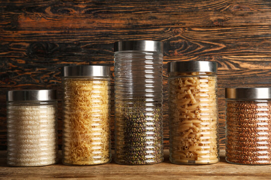 Glass jars with different products on brown wooden background