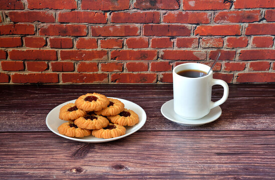 Kurabye, Azerbaijani shortbread cookies with fruit jam, on a plate and a cup of hot tea on a wooden table.