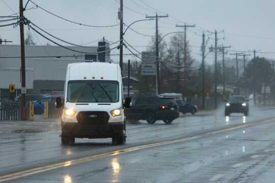 La Tuque, Canada, 07 May 2026 : A white Ford Transit van drives on a wet road with its headlights on during a rainy day.