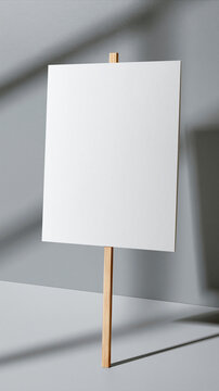 A blank white paper sign is attached to a piece of wood, with the shadow of a building's window cast on the wall.
