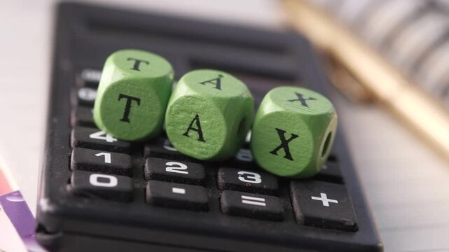 Tax concept showing green wooden cubes with 'tax' lettering on calculator, emphasizing financial planning and income taxation with dynamic motion