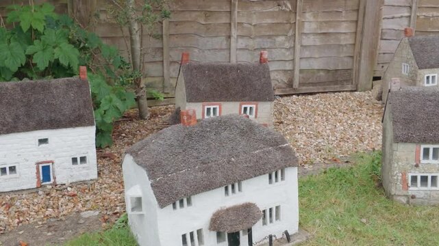 Model thatched cottages at Godshill Model Village as camera pans right past miniature stone houses, textured roofs, tiny windows and doors, outdoor garden display on Isle of Wight, UK.