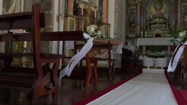 White ribbon and flowers decorate a wooden pew beside the aisle of a gilded church altar