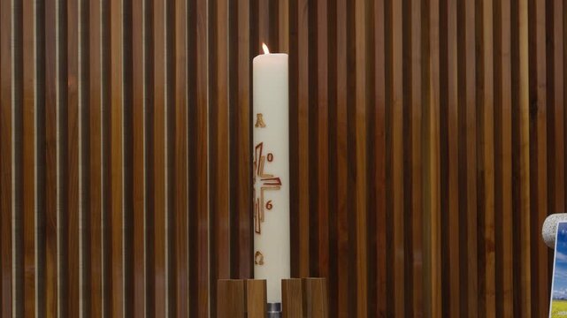 Tall white church candle with cross and alpha omega symbols indoors