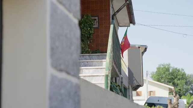 Portuguese flag hanging from a house balcony along a residential street in Portugal