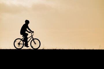 Obraz premium Minimalist silhouette of a cyclist riding a bicycle along a clean horizon under a warm twilight sky ideal for concepts of eco-friendly transport healthy living balance and freedom.