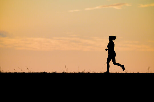 Silhouette of a woman jogging against a vibrant golden hour sunset sky highlighting athletic training healthy living endurance outdoor exercise and personal achievement in a serene setting.