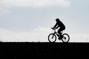 Obraz premium High-contrast profile silhouette of a cyclist riding a bicycle along a hilltop trail under an expansive sky illustrating outdoor recreation active transportation fitness eco-friendly commuting and