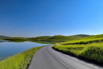 Obraz premium Scenic Lakeside Road Through Rolling Green Hills Under Blue Sky