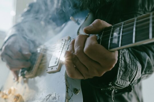 Close up of a musicians hands playing a worn electric guitar with a leather jacket and soft hazy light for music and entertainment concepts