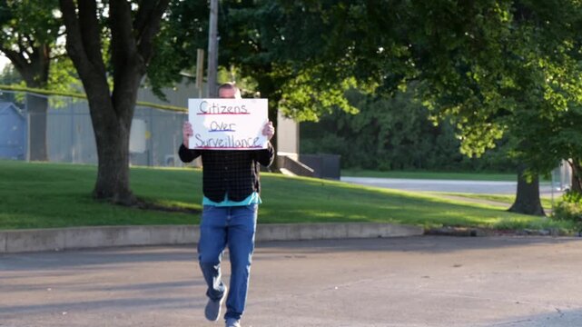 Demonstrator holding a Citizens Over Surveillance sign, protesting mass tracking, license plate readers, Fourth Amendment overreach illegal search
