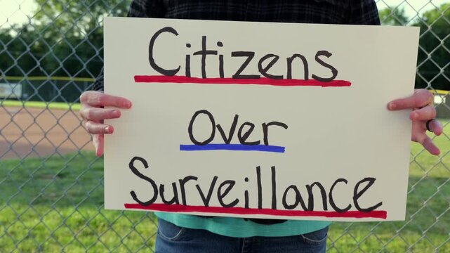 Demonstrator holding a Citizens Over Surveillance sign, protesting mass tracking, license plate readers, Fourth Amendment overreach illegal search