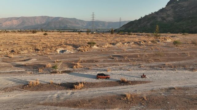 Aerial Orbiting Shot of an SUV and Motorcycle Driving on a Dry Lahar Dirt Trail