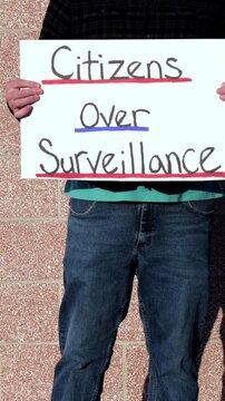 Demonstrator holding a Citizens Over Surveillance sign, protesting mass tracking, license plate readers, Fourth Amendment overreach illegal search