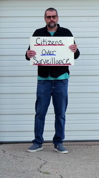Demonstrator holding a Citizens Over Surveillance sign, protesting mass tracking, license plate readers, Fourth Amendment overreach illegal search