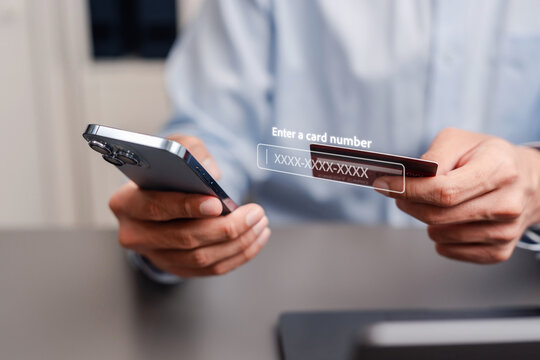 Entering credit card number for online payment. Man holding smartphone and bank card with virtual data entry interface.