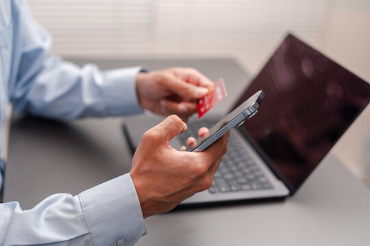 Online payment and e-commerce shopping concept. Man holding credit card and using smartphone at desk with laptop.