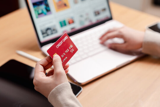 Online shopping and digital payment concept. Hand holding a red credit card while typing on laptop keyboard.
