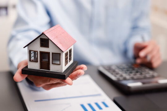 Real estate investment and mortgage concept. Hand holding model house with calculator and financial documents.