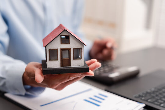 Real estate investment and mortgage concept. Hand holding model house with calculator and financial documents.
