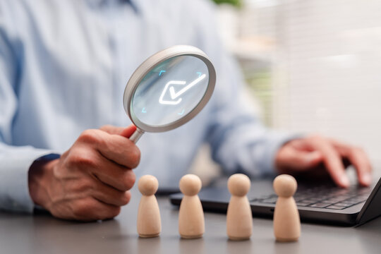 Recruitment and talent acquisition concept. Businessman using magnifying glass with checkmark to select wooden figure.