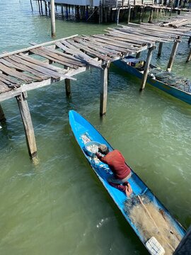 Fisherman working on his blue wooden boat near an old rustic pier in a traditional stilt village