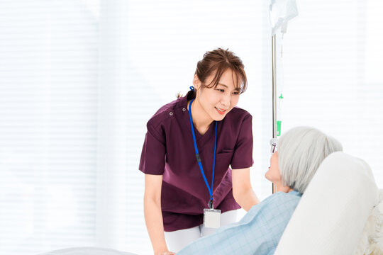リクライニングベッドにいるシニア女性患者と看護師,介護士の女性スタッフ（医療イメージ）