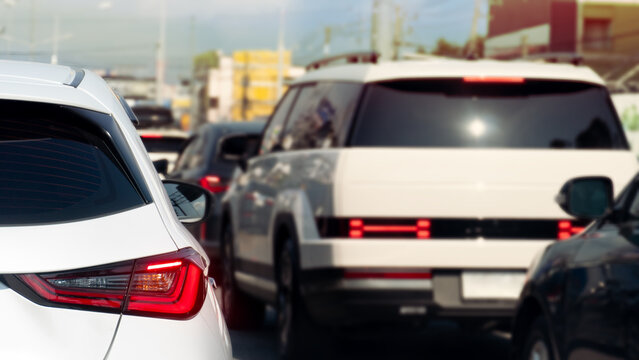 Rear view of modern cars stopped in a heavy traffic congestion during the daytime. Scene captures the bright red tail lights and sleek automotive designs queued up on a city road at Thailand.