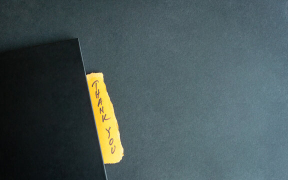 Handwritten Thank you on yellow paper slit between a notepad
