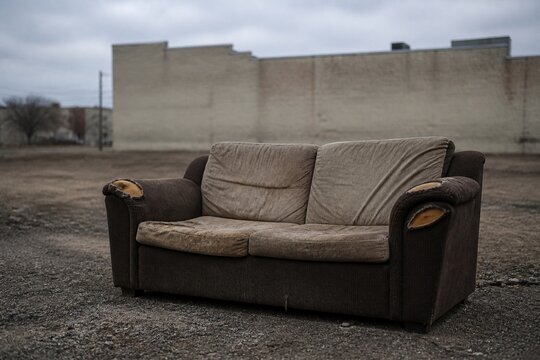A worn-out sofa on an empty urban lot, overcast daylight.