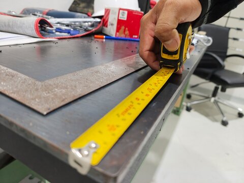 A close-up view of a craftsman using a yellow measuring tape to check dimensions on a metal workbench