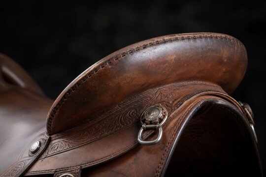 Close-up of a western saddle's leather cantle with metal fittings on dark background.