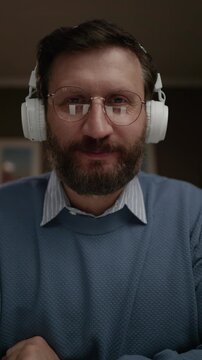 Man wearing headphones looking at camera and modestly smiling while waving in greeting. Close-up