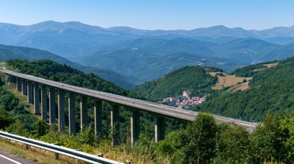 Naklejka premium Expansive View of a Modern Highway Bridge Above Lush Green Hills with Mountains in Distance Under Clear Blue Sky