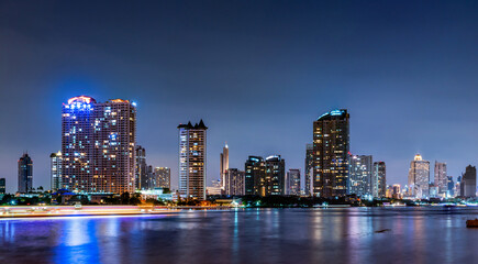 Panoramic Bangkok cityscape at night featuring illuminated skyscrapers beside Chao Phraya River. Urban architecture in Thailand modern capital. Modern waterfront architecture. Metropolitan landscape. © Fahroni