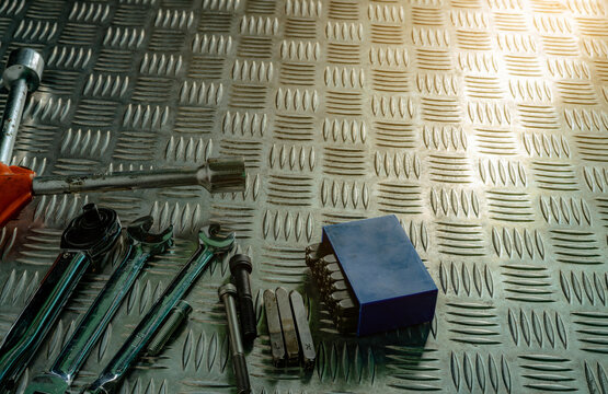 Professional mechanic tools including ratchet wrench, spanners, hex key set and bolts arranged on textured steel checker plate for industrial maintenance and engineering backgrounds.