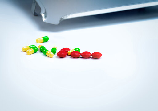 Red tablets and green-yellow capsules pills with drug tray on white table. Pharmaceutical industry. Vitamins and supplements. Pharmaceutics concept. Pharmacy products. Healthcare and medication.