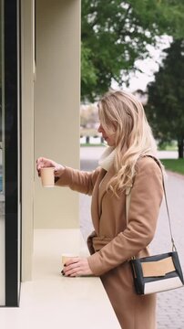 Vertical video. Coffee kiosk. Customer buying. Woman in coat ordering in autumn park street cafe hot beverage adding cinnamon to drink.