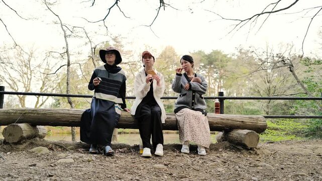 Three women relax on a wooden bench. They smile, laugh, and gesture with joy. Nature frames their peaceful, candid moment. Perfect for lifestyle, travel, or community scenes. No animals, no plants