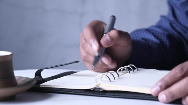 Close up motion of person writing in notebook with pen, showcasing process of taking notes during meeting or study session