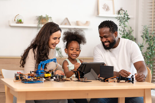 family help kid assembling a DIY robot kit and circuit board on desk,sharing a happy smile while a daughter working on a school technology project