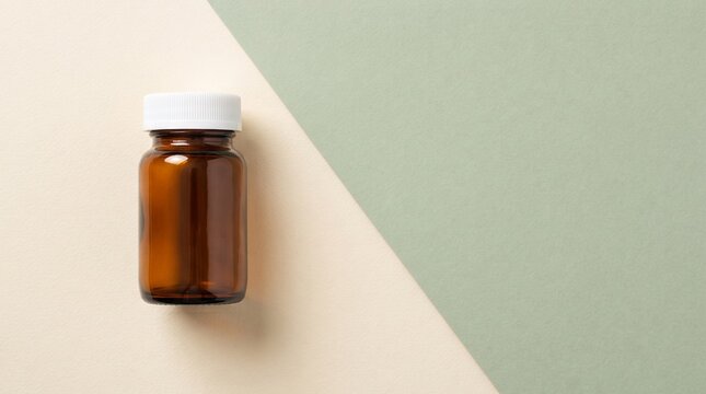 Empty amber glass pill bottle with white cap on a split beige and green background