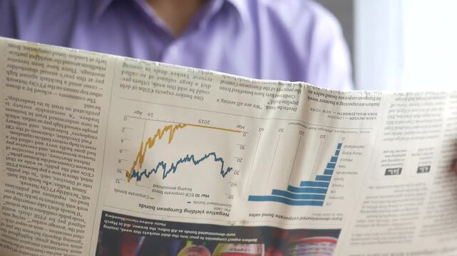 Close up of man reading financial newspaper with stock market charts and business news articles