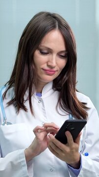 Beautiful female doctor in a white coat with a stethoscope around her neck using her smartphone for messaging, scrolling, or online medical consultation, modernizing healthcare services