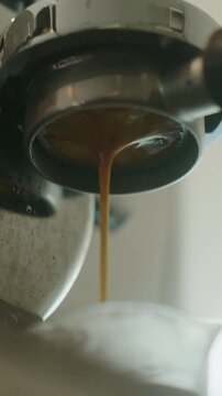 Close up of espresso extraction from bottomless portafilter into white cup.