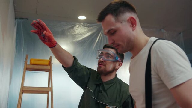 NEW YORK - April 5, 2017: Positive, smiling young repairers at the workplace discussing the results of their work, one of them points at the wall, they laugh at it, the worker in goggles slaps the