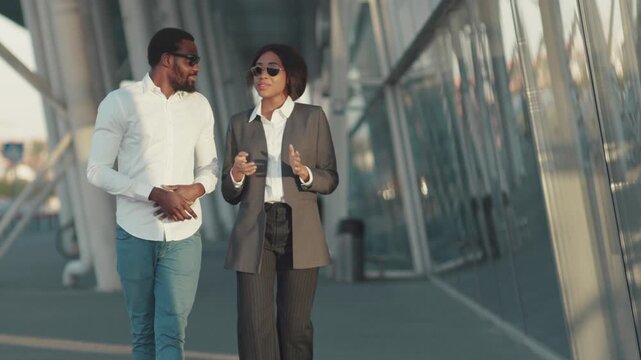 Young Afro-American couple in formal outfits walking outside the office having a business conversation, smiling, gesturing and shaking their hands. Business, contract, having a deal. Successful