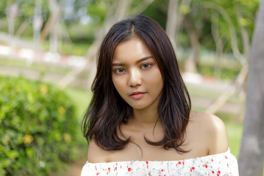 Close up portrait of beautiful young Asian woman looking at camera in green park. Natural daylight with shallow depth of field, suitable for beauty, lifestyle and outdoor concepts.