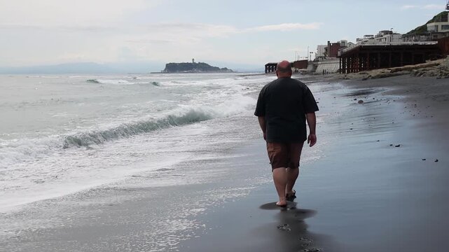 Person walking barefoot along the beach in Kamakura, Japan, with gentle ocean waves, wet sand and Enoshima island visible in the distance. Peaceful coastal travel scene. Big man on a sea.