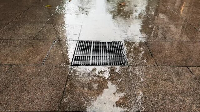 Large Metal Storm Drain Grate Flooded tiles Sidewalk during Tropical Rainstorm